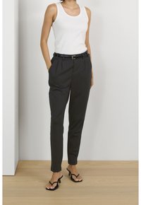 Pantalons noirs sur mesure avec des plis à l'avant, associés à un top sans manches blanc. Finition avec une ceinture noire et portés avec des sandales à talons noires.