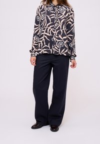 Bluzka na długi rękaw zapinana na guziki, z granatowo-beżowym wzorem liści. Lekka tkanina, kołnierzyk z ozdobnymi guzikami, zestawiona z ciemnymi, szerokimi spodniami.