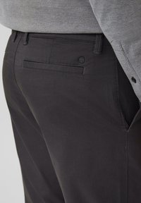 Gros plan sur une personne portant un pantalon gris foncé sur mesure et une chemise texturée gris clair avec des poignets boutonnés.
