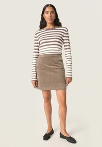 Stripet langærmet top i creme og brune nuancer, parret med en brun cord-skirt. Sorte flade sko fuldender outfittet.