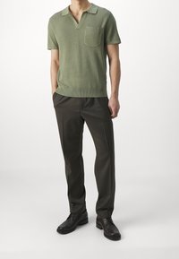 Vihreä neulottu poolopaita, jossa on lyhyet hihat ja tasku, yhdistetty tummanruskeisiin räätälöityihin housuihin ja mustiin juhlakenkiin.