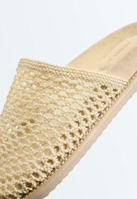Beige instapsandaal met geweven bovenwerk en gevoerde binnenzool, voorzien van een textuurrijke zool voor grip.