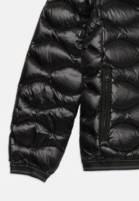 Fekete pufferezüst, párnázott hullámokkal, texturált nylon anyagból készült, rugalmas mandzsettákkal és cipzáras oldalzsebbel.