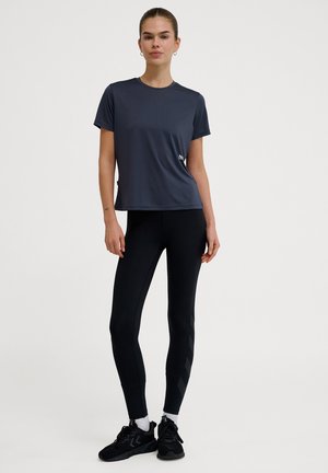 Grå kortærmet træningsskjorte med rund halsudskæring, parret med sorte leggings med et diskret mønster langs siderne.
