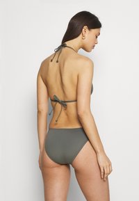 Dark olive green bikini with a halter neck design, tie-back closure, and minimalistic style. Smooth texture and medium coverage bottoms.