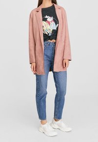 Blazer en Suède rose sur un t-shirt graphique noir, associé à un jean taille haute bleu clair et des baskets blanches.