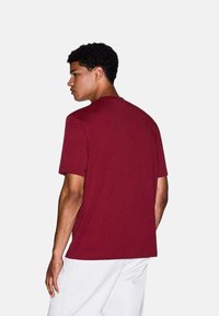 Bordeaux-kleurige katoenen T-shirt met korte mouwen en een ronde halslijn, met een relaxte pasvorm en een gladde textuur, gezien vanuit de achterkant.