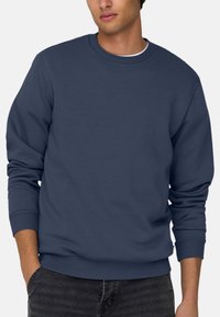 Sweatshirt en coton bleu marine avec un col ras du cou, des poignets et un ourlet côtelés. Texture douce, design décontracté, sans logos ni motifs visibles.