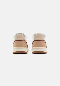Pantofi sport cu un superior din suede bej, accente din piele albă și detalii mahon. Talpă din cauciuc solid cu stropi subtile. Vedere din spate prezentată.
