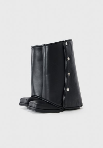Bottes noires montantes en cuir lisse avec un bout arrondi, dotées d'un design replié et d'accents à bouton-pression sur les côtés.