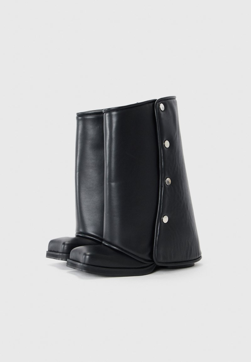 Bottes noires montantes en cuir lisse avec un bout arrondi, dotées d'un design replié et d'accents à bouton-pression sur les côtés.