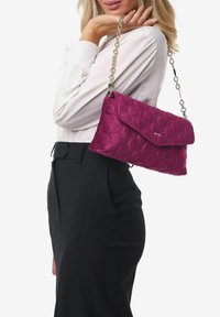 Borsa a tracolla trapuntata viola con chiusura a pattina e tracolla a catena. Presenta motivi floreali in rilievo e una texture liscia. Design compatto e strutturato.