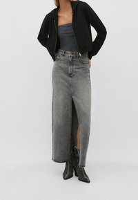 Haut noir coupé avec poches avant, associé à une jupe en denim gris taille haute avec une fente sur le côté. Le mannequin porte des bottes noires texturées.