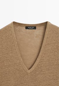 Pull marron à col en V avec une texture en maille fine et une étiquette noire portant l'inscription "Massimo Dutti Made in Cambodia" à l'intérieur du col.