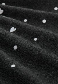 Schwarzer Stoff mit einer sanften Textur, der mit weißen gestickten Herzen und kreisförmigen Mustern bedeckt ist, die über die Oberfläche verstreut sind.