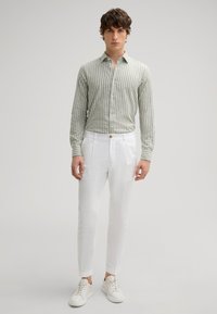 Hellgrünes gestreiftes Hemd, weiße Leinenhose und weiße Sneakers. Slim Fit, Button-Down-Kragen und strukturierter Stoff. Minimalistisches Design.