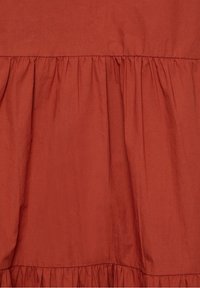Prenda de color óxido con detalles fruncidos a lo largo del dobladillo, hecha de una tela texturada. Superficie suave y lisa con un brillo sutil.