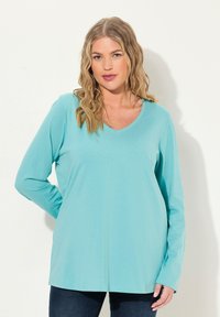 Hellblaues Langarmtop mit V-Ausschnitt, weicher Textur und lockerer Passform, kombiniert mit dunklen Jeans. Keine sichtbaren Muster oder Akzente.