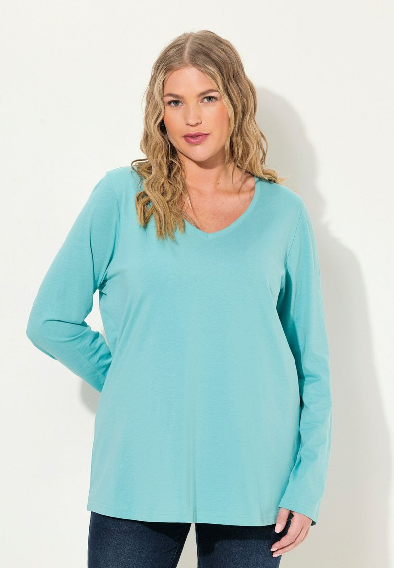 Hellblaues Langarmtop mit V-Ausschnitt, weicher Textur und lockerer Passform, kombiniert mit dunklen Jeans. Keine sichtbaren Muster oder Akzente.