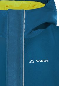 Blauwe waterdichte jas met een gele voering, voorzien van een rits aan de voorkant en reflecterende accenten. Logo prominent op de borst weergegeven.