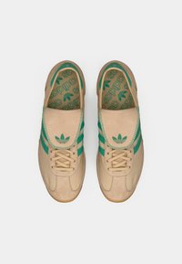 Μπεζ αθλητικά παπούτσια με πράσινες λεπτομέρειες, με επάνω μέρος από σουέντ, κλείσιμο με κορδόνια και λαστιχένια σόλα. Το εσωτερικό διαθέτει πράσινη πέλμα με σχέδιο.