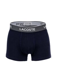 Ανδρικά σκούρα μπλε boxer briefs με γκρι ελαστική ζώνη που έχει το λευκό λογότυπο Lacoste και ένα μικρό έμβλημα κροκόδειλου στην εσωτερική ετικέτα.