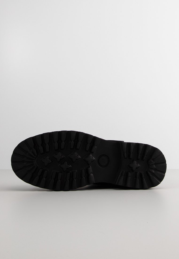 Suela de bota de goma negra con un patrón de banda de rodadura que presenta surcos profundos y secciones elevadas para mejorar la tracción. Forma plana y ancha con bordes redondeados.