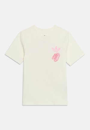 T-shirt blanc à manches courtes avec un logo Adidas rose et un graphisme de baskets roses sur le côté gauche de la poitrine.