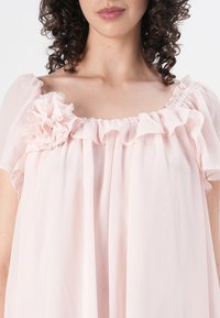 Šviesiai rožinė, permatoma, plazdanti suknelė su volantine iškirpte ir subtiliu gėlių akcentu kairiajame petyje. Minkšta tekstūra ir per didelis siluetas.