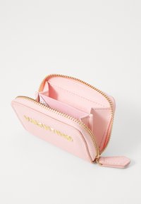 Petit portefeuille en cuir synthétique rose avec zip doré, logo en relief, deux emplacements pour cartes et finition texturée. Intérieur doublé en rose assorti.