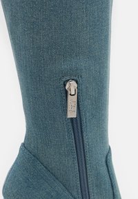 Blå denim ankelboot med en sidodragkedja, försett med en metallisk draggrepp. Texturerad tyg och en slank, konturerad silhuett.