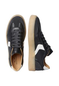 Sneaker in pelle nera con un design imbottito, caratterizzate da un accento bianco, lacci grigi e suola in gomma color caramello. Dettaglio testurizzato sul tallone incluso.