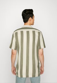 Camisa de manga corta con rayas verticales en verde oliva y crema, con cuello tipo muesca y un corte relajado, fabricada en tejido ligero.