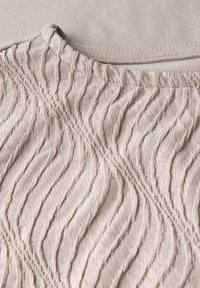 Tela beige con un patrón texturizado en forma de olas y una capa suave y contrastante por debajo. Material suave y elástico, con bordes acabados.