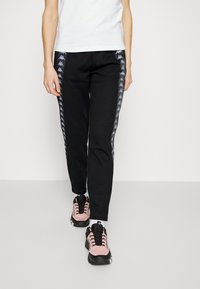 Svarta träningsbyxor har en slim fit och Kappa-logotape längs sidorna. Kombineras med rosa och svarta sportskor. Vit tröja ovanpå.