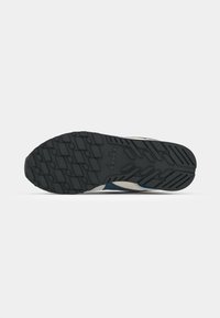 Black rubber outsole with a textured grip pattern. Light-colored upper with blue and red accents and textured side panels. Circular toe shape.