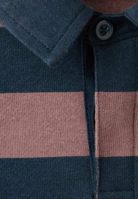 Gros plan sur le col d'un polo tricoté rayé bleu marine et rose, avec un bouton et des coutures détaillées.