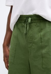 Πράσινο, ελαφρύ παντελόνι μ�ε ελαστική μέση και κορδόνι. Διαθέτει πλαϊνές τσέπες και ορατές ραφές.