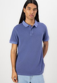 Blue cotton polo shirt with a collar, two-button placket, short sleeves, subtle logo on the left chest, and a straight hem.