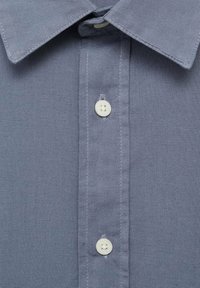 Camicia button-down azzurro chiaro con colletto classico, due bottoni bianchi e un tessuto testurizzato con sottili dettagli di cucitura.