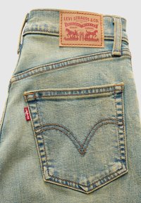 Φωτεινό μπλε τζιν παντελόνι με ταμπέλα από δέρμα ταμπά στη μέση. Διαθέτει πίσω τσέπη με χαρακτηριστική ραφή σε σχήμα V και κόκκινη ταμπέλα Levi's.