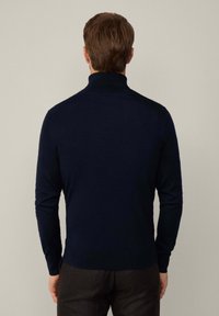 Mörkblå stickad tr�öja med hög krage, långa ärmar, figurnära design och ribbade ärmslut och fåll, uppvisad bakifrån.