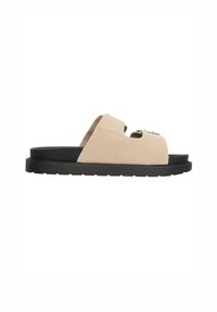 Beige mockasin sandal med öppen tå, med en enkel svart sula och en framträdande metallaccent på ovansidan.