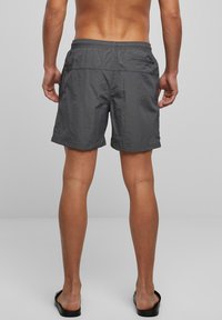 Grå badebukser laget av lett materiale, med elastisk midjebånd, sidelommer og en baklomme med glidelås for oppbevaring.