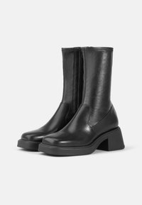 Bottines en cuir noir avec une texture lisse, présentant une fermeture éclair sur le côté, un bout arrondi et un talon épais pour plus de hauteur.
