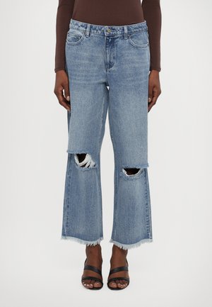 Jeans a gamba larga in denim blu chiaro con orli sfrangiati e ampie aperture sulle ginocchia. Design a cinque tasche con chiusura a bottone e passanti per cintura.