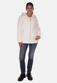 Giacca impermeabile bianca con cappuccio, dotata di una cerniera frontale e tasche laterali. Indossata con jeans blu e scarpe nere.