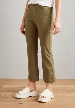 Pantalons cropped verts olive avec coupe ajustée, fermeture à bouton et poches arrière. Associés à des chaussures à plateforme blanches à enfiler.