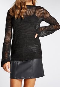 Maglione nero a maglia con un tessuto aperto e testurizzato, maniche lunghe e scollatura rotonda, abbinato a una minigonna nera in pelle.