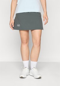 Dark gray sports skirt with a fitted design, featuring an EA7 logo on the side. The model wears white socks and sneakers.